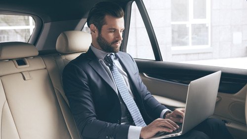 Business traveller working on a laptop in the back seat of an executive car