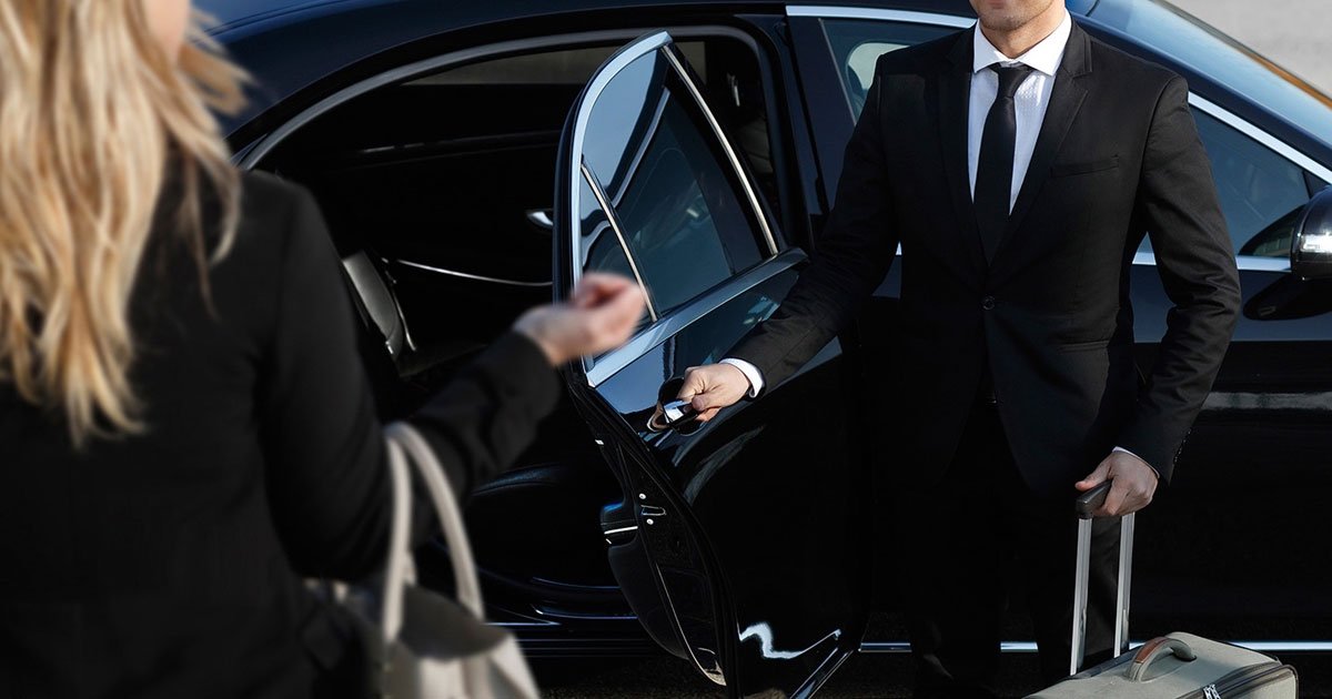 Chauffeur in a suit opening the door of a black executive car for a passenger